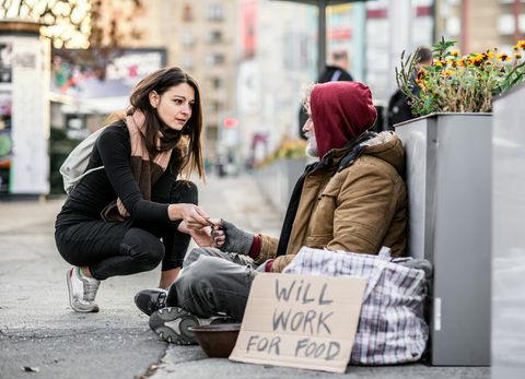 Ung kvinde giver penge til hjemløs tigger mand sidder i byen.