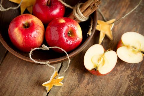 Modne friske røde æbler i skål med kanel på træbaggrund. Efterår høst. Juledekoration