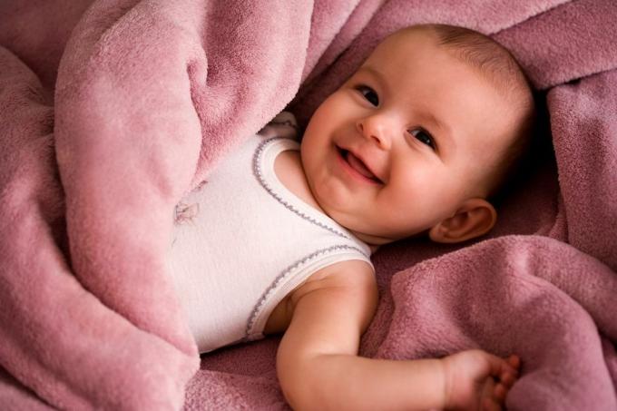 portræt af baby i en hvid tank-stil skjorte smilende og pakket ind i et blødt pink tæppe