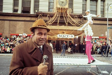 joe garagiola taler i mikrofon med akrobater i baggrunden ved Macys Thanksgiving Day parade i 1970