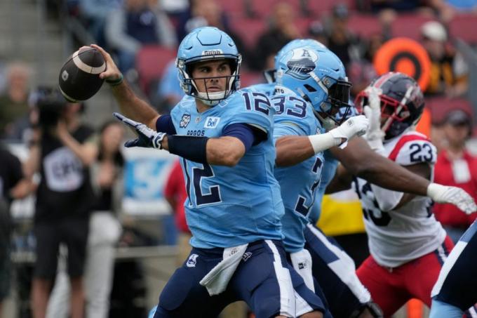 canadisk fodbold quarterback i blå uniform kaster en aflevering, da den offensive linje holder en defensiv spiller i rød og hvid