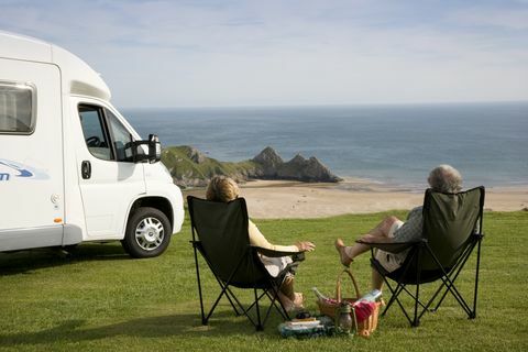 Et par med en picnic slapper af i deres stole ved siden af ​​deres autocamper og nyder udsigten over Three Cliffs Bay på Gower-halvøen i Wales., Three Cliffs Bay, Swansea, Wales.