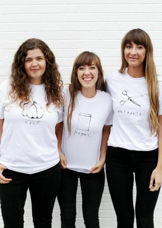 tre kvinder i hvide t-shirts, med enten sten, papir eller saks skrevet og afbildet på skjorten