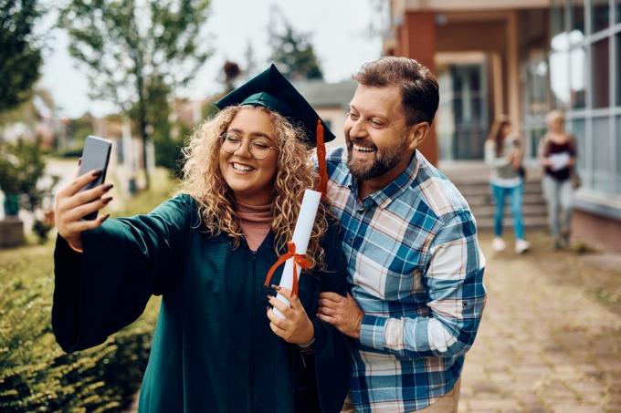 glad universitetsuddannet og hendes far hygger sig, mens hun tager selfie med smartphone