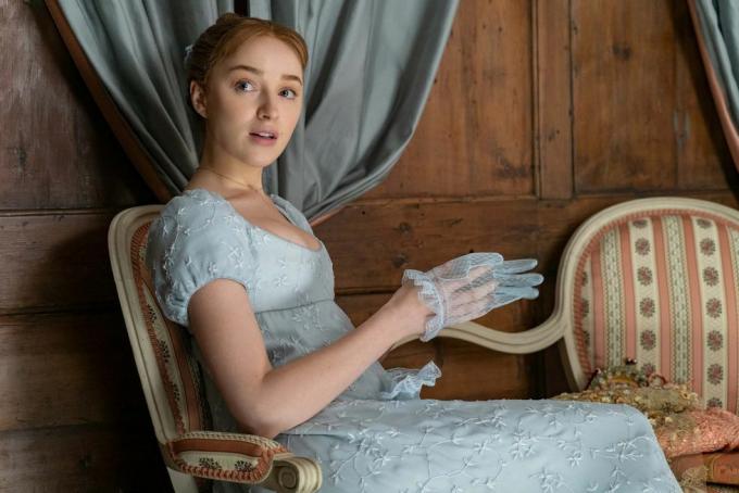 phoebe dynevor som daphne bridgerton i afsnit 102, siddende, iført en blå, empire-taljet kjole