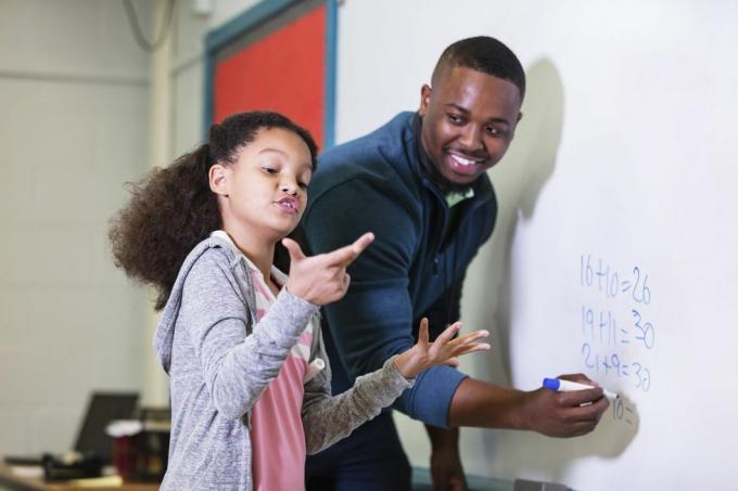 en multiraciel 9-årig pige i matematiktime, der står ved tavlen med sin lærer, en ung afroamerikansk mand i sin 20'erne kigger læreren på sin folkeskoleelev og venter, mens hun forsøger at finde ud af svaret, fokus er på pige