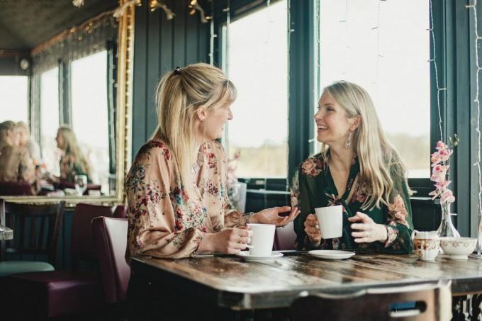 et billede forfra af to smukke midt voksne kvinder, der nyder kaffe sammen på en cafe, de sidder ved et bord og griner med hinanden