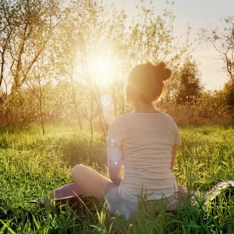 ung kvinde sidder i yogastilling og nyder solnedgang i naturen