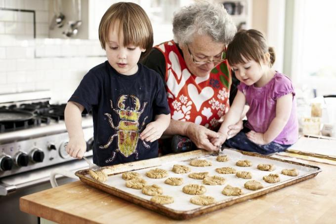 bedstemor og to små børnebørn bager barnebarnet placerer dejen på en bageplade med bedstemødres hjælp