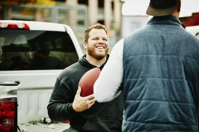 smilende mand, der holder fodbold, hænger ud med en ven under tailgating-fest