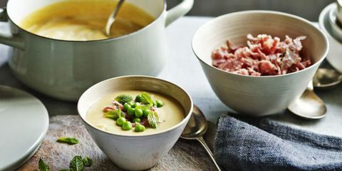 Del ærter og skinke suppe i skål med frisk mynte sammen med skål med revet skinke